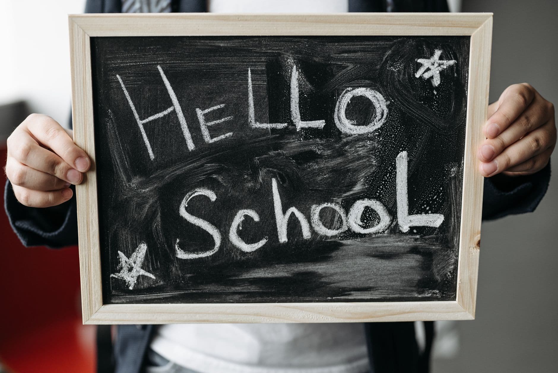 Hands holding a wooden-framed chalkboard with “Hello School” written in white chalk.