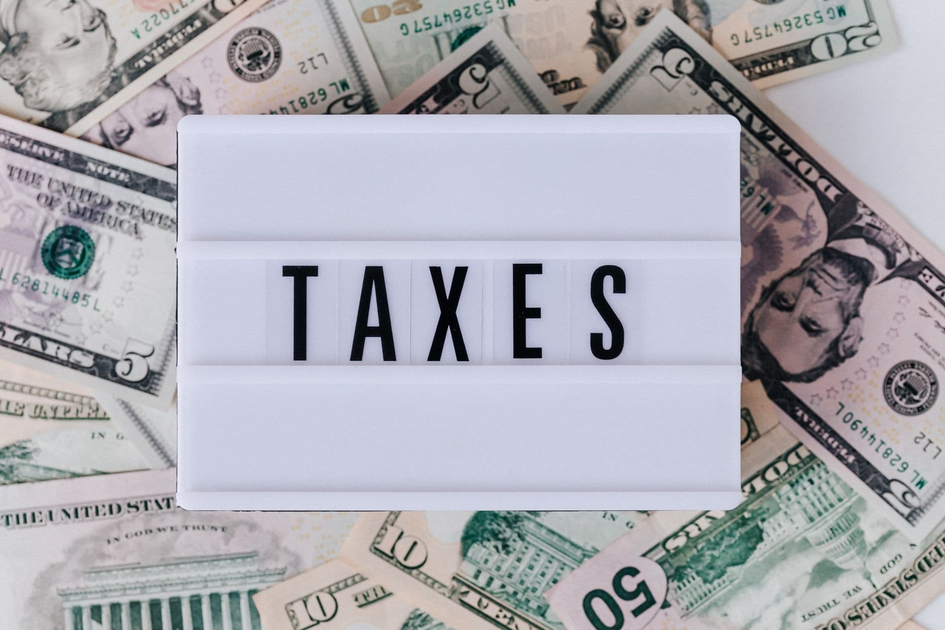 Lightbox spelling TAXES surrounded by scattered U.S. dollar bills.