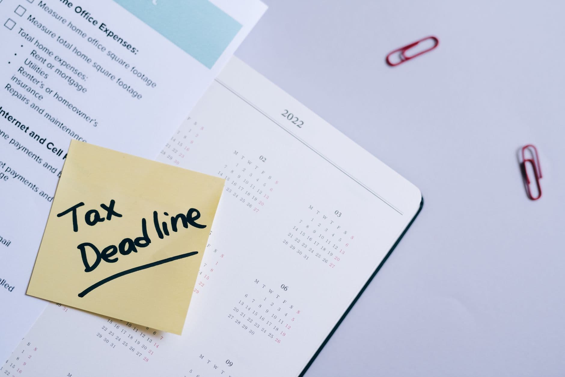 Yellow note reading “Tax Deadline” on a 2022 calendar with paperwork and red paper clips.