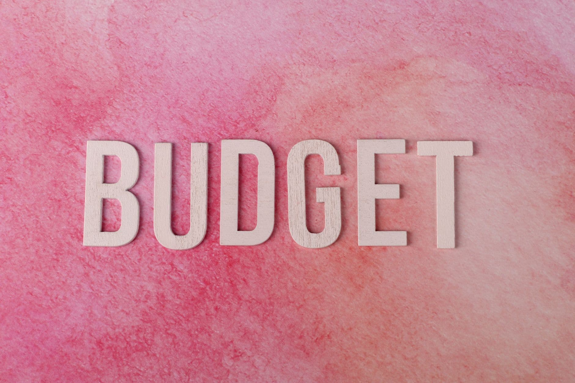 The word “BUDGET” in wooden letters on a pink textured background.