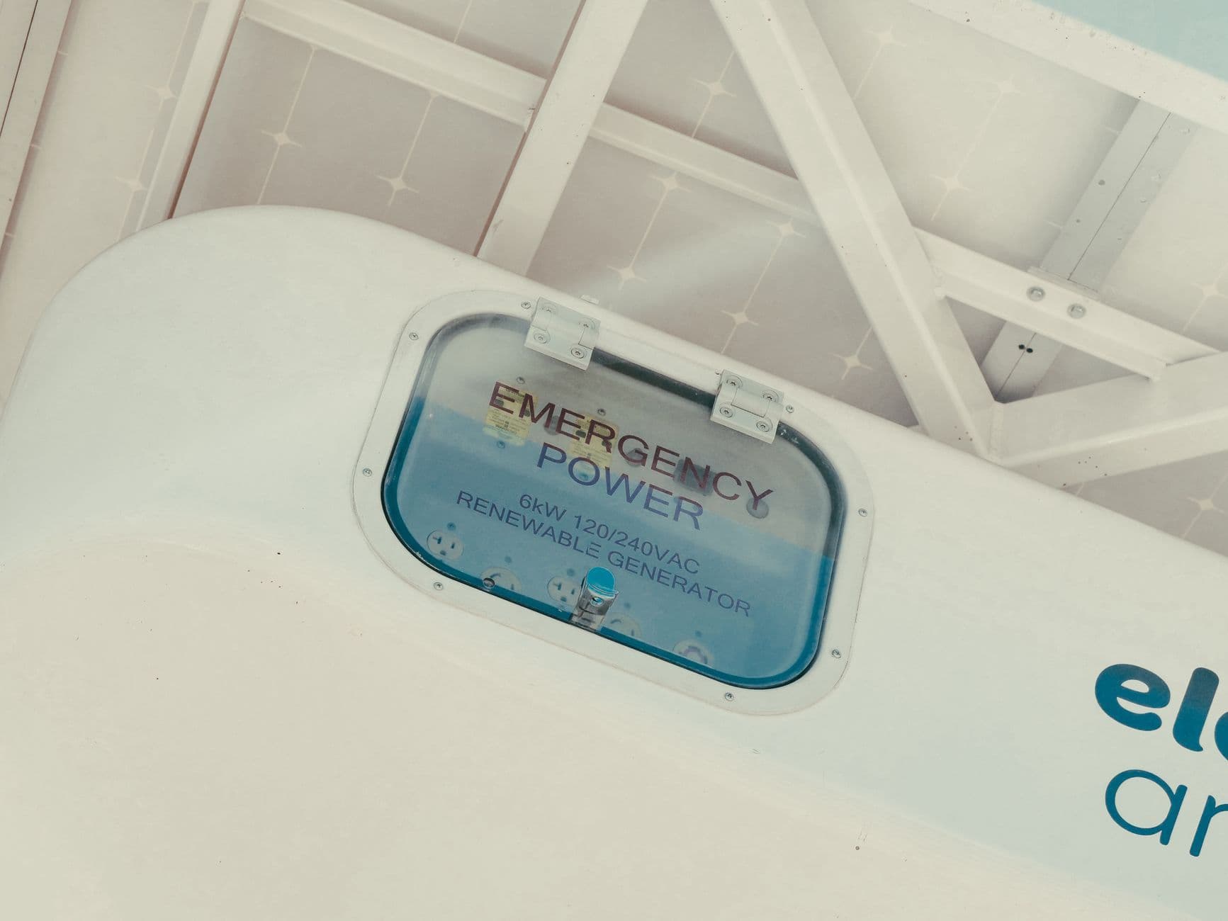 Close-up of an emergency power enclosure labeled for a 6-kilowatt renewable generator beneath solar panels.