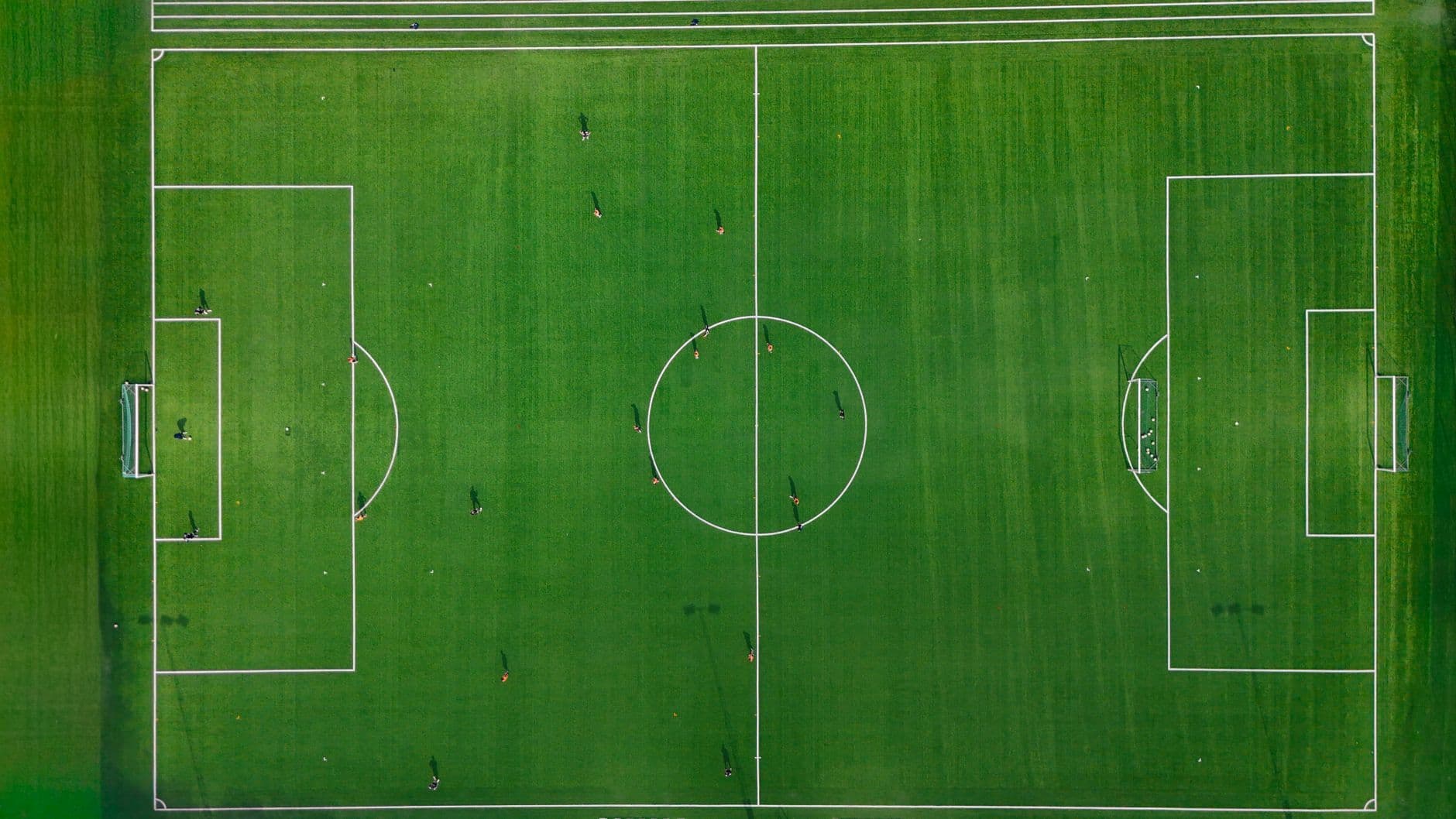 Overhead view of soccer players on a green field with white boundary lines, goals and a center circle.
