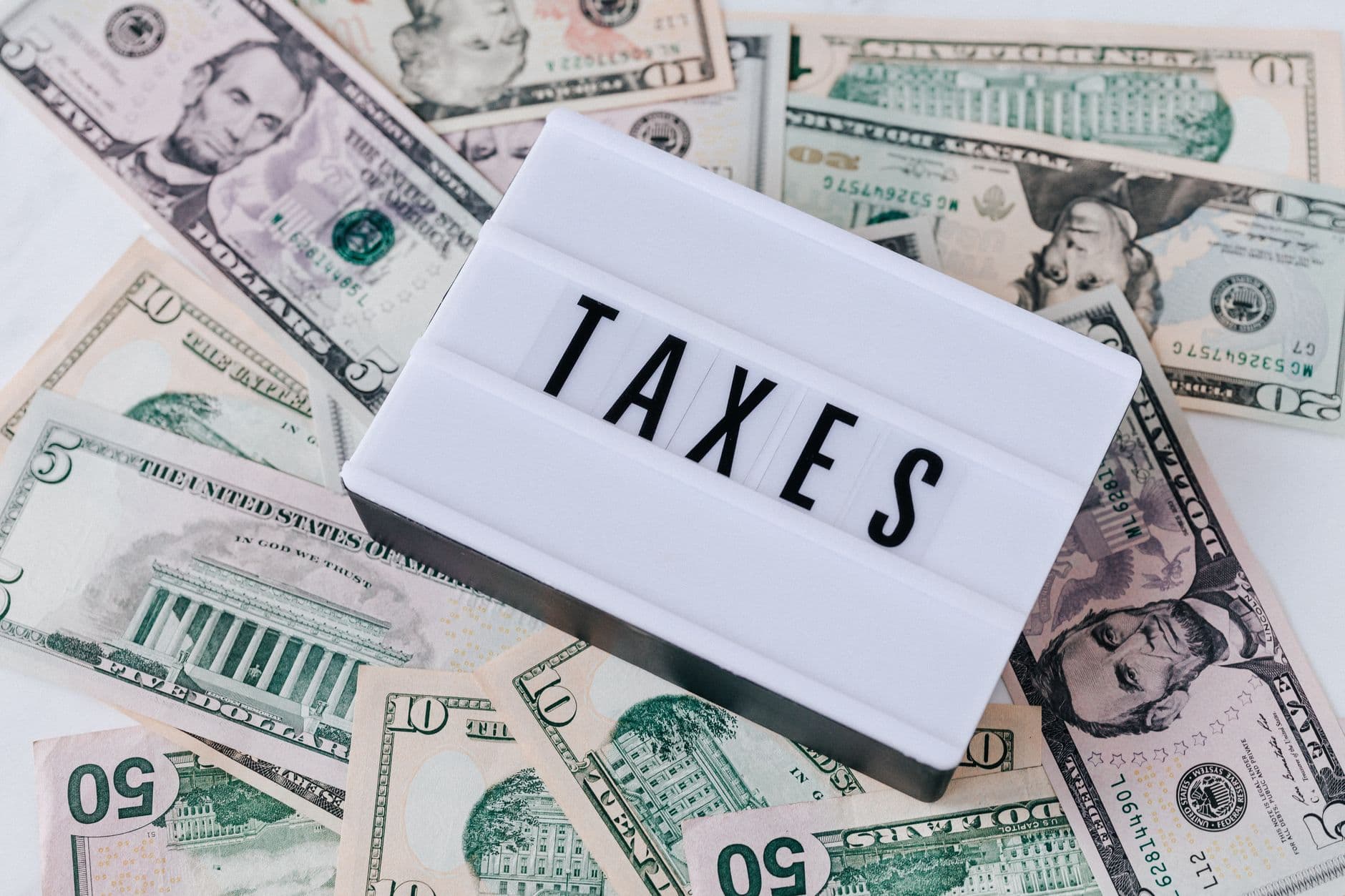 Lightbox with the word “TAXES” surrounded by scattered U.S. dollar bills.