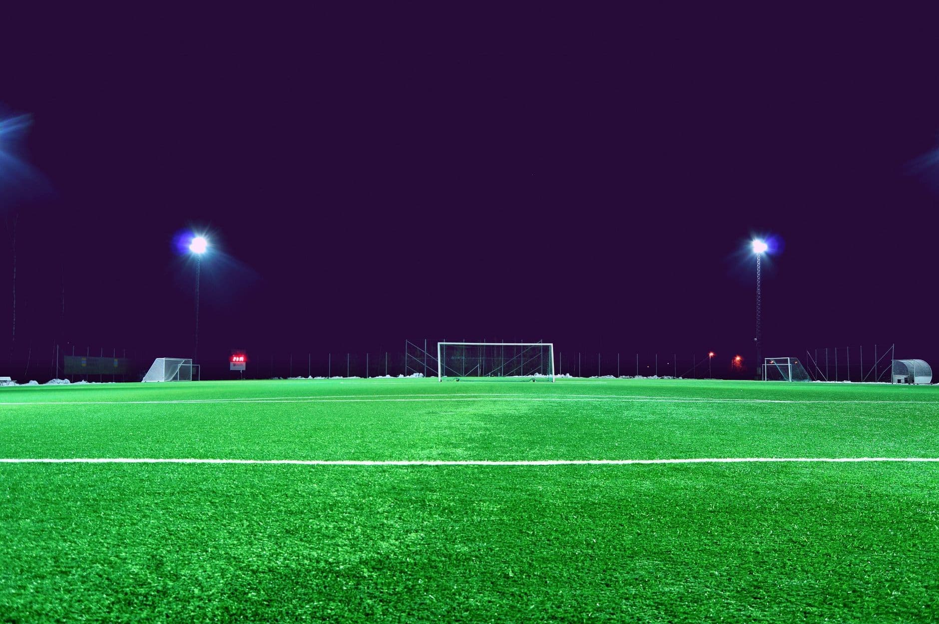 Empty green soccer field with goals under bright floodlights at night.