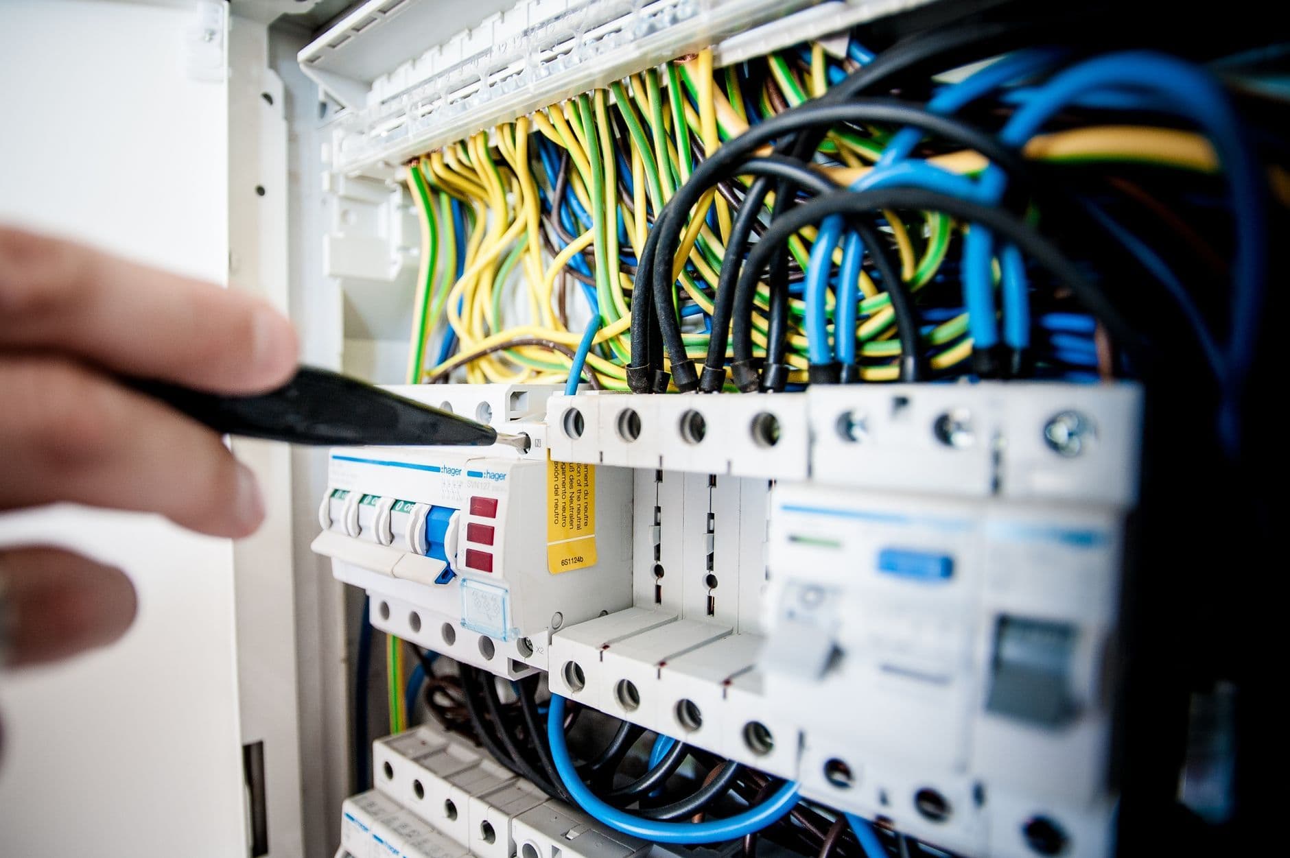 Close-up of a hand using a screwdriver on a breaker in an open electrical panel.