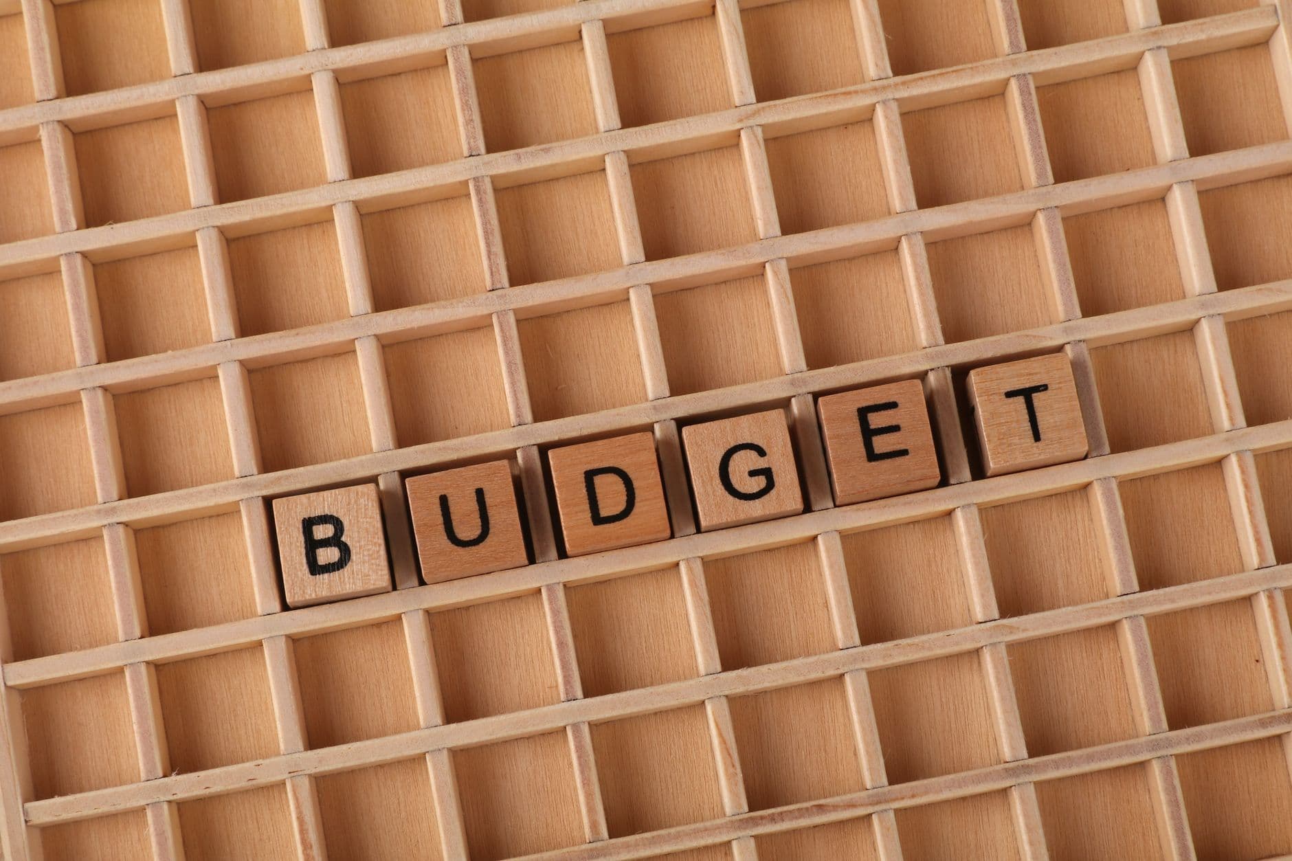 Wooden tiles spelling BUDGET arranged in a compartmented wooden tray.