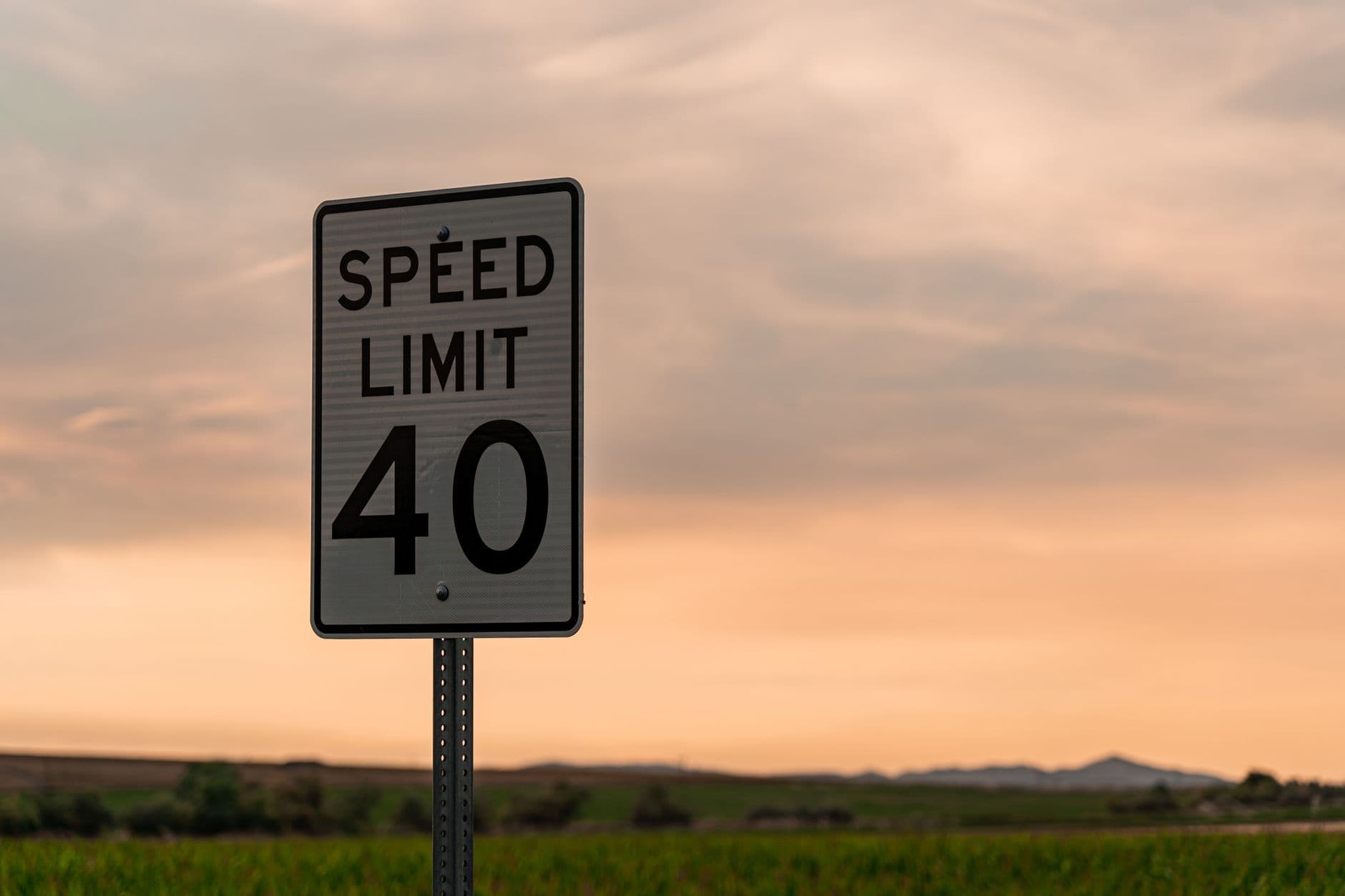 Speed limit 40 sign against a warm sky with fields in the background.