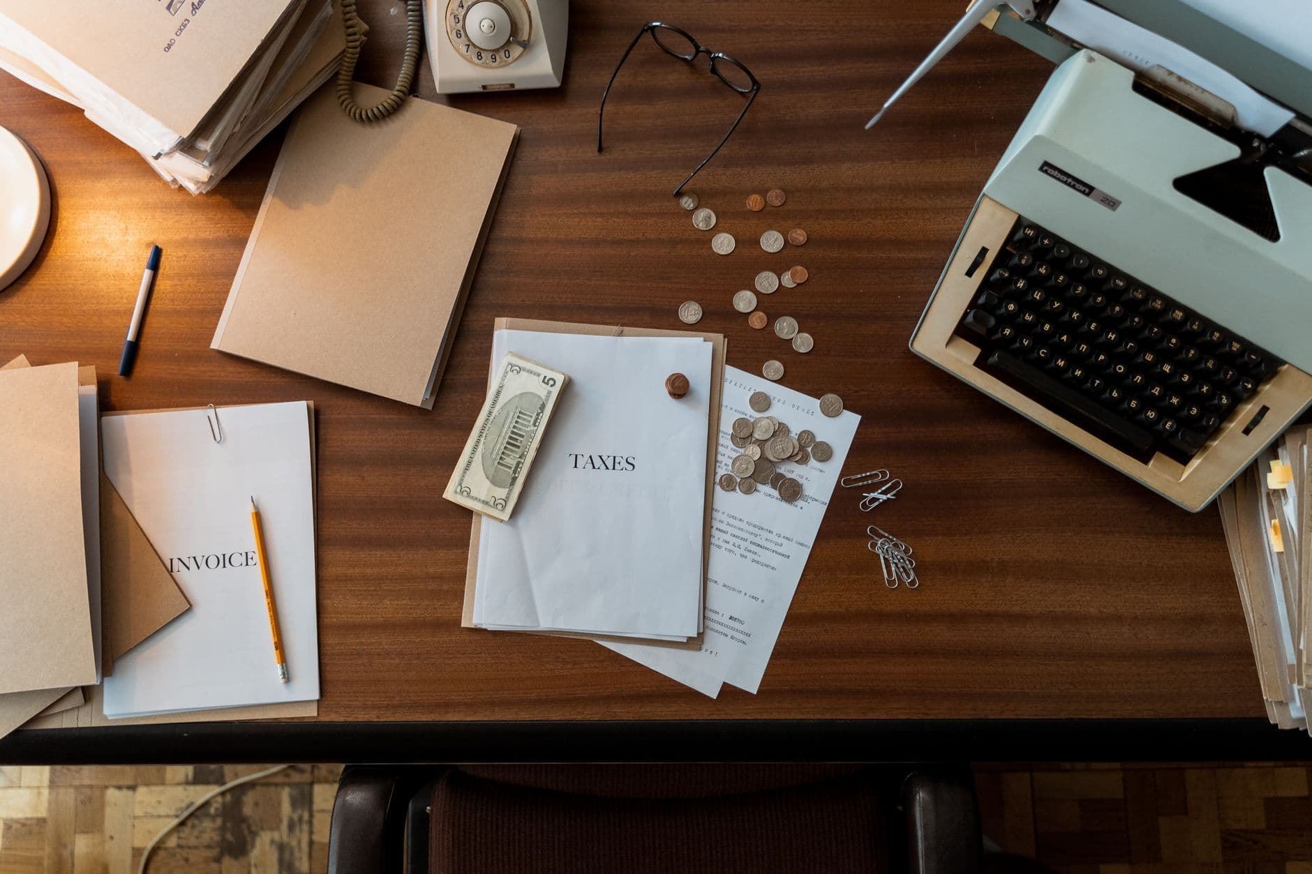 Overhead view of a desk with tax and invoice papers, cash, coins, folders, a telephone and a typewriter.