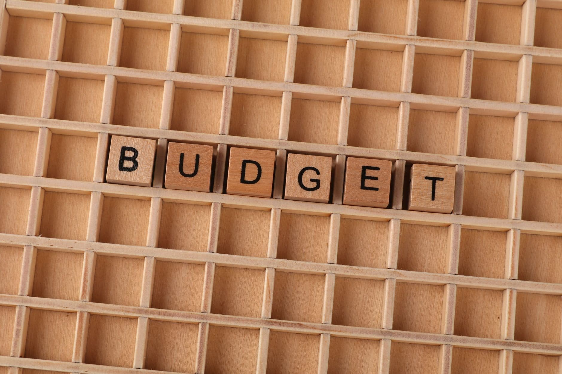 Wooden tiles spelling budget arranged in a compartmented wooden tray.