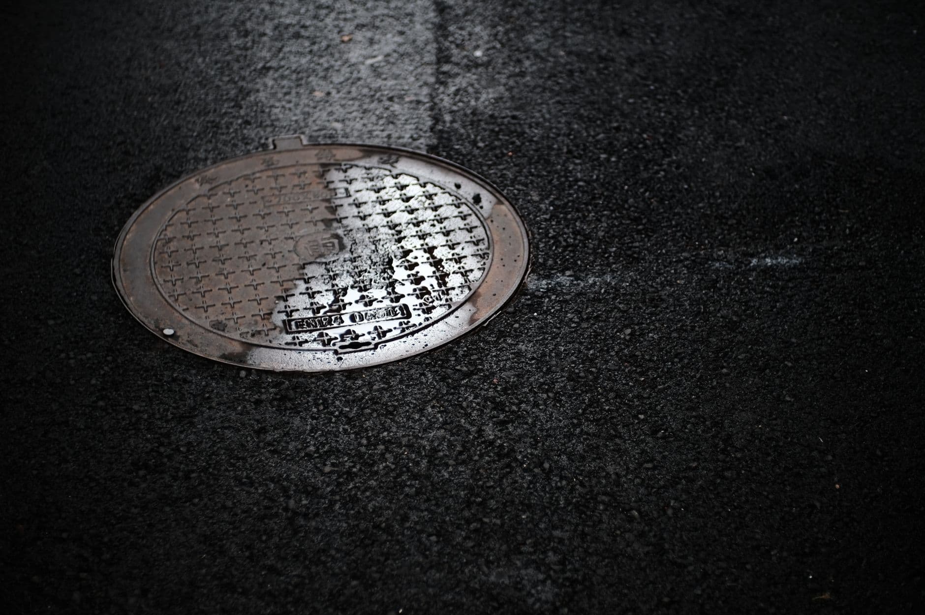 Round metal utility access cover on wet black asphalt.