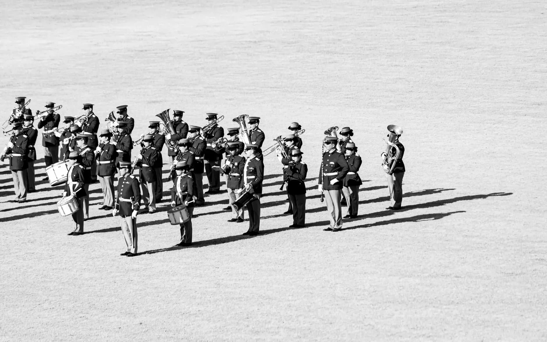 Black-and-white wide view of a uniformed band holding brass, woodwind and percussion instruments on an open field.