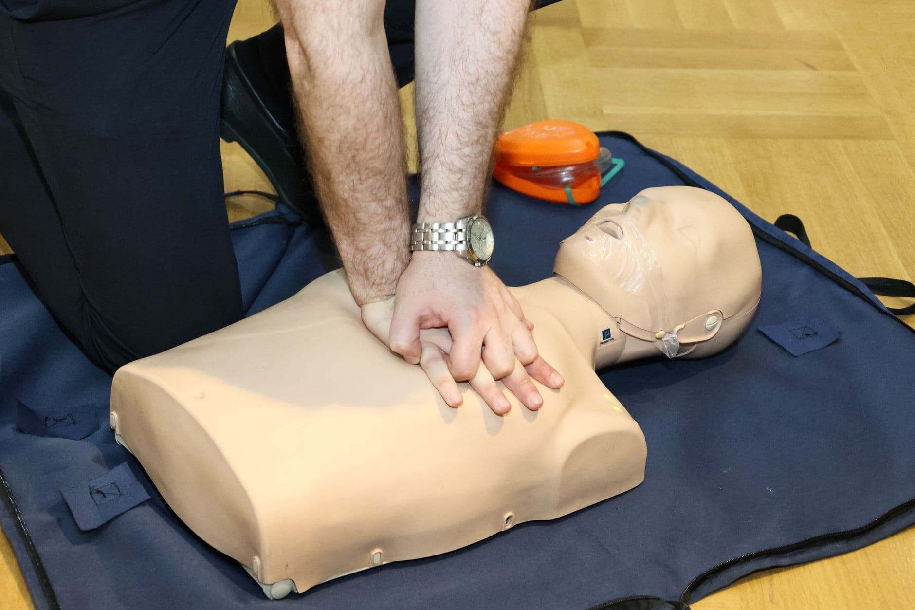 Hands performing chest compressions on a CPR training mannequin placed on a padded mat.