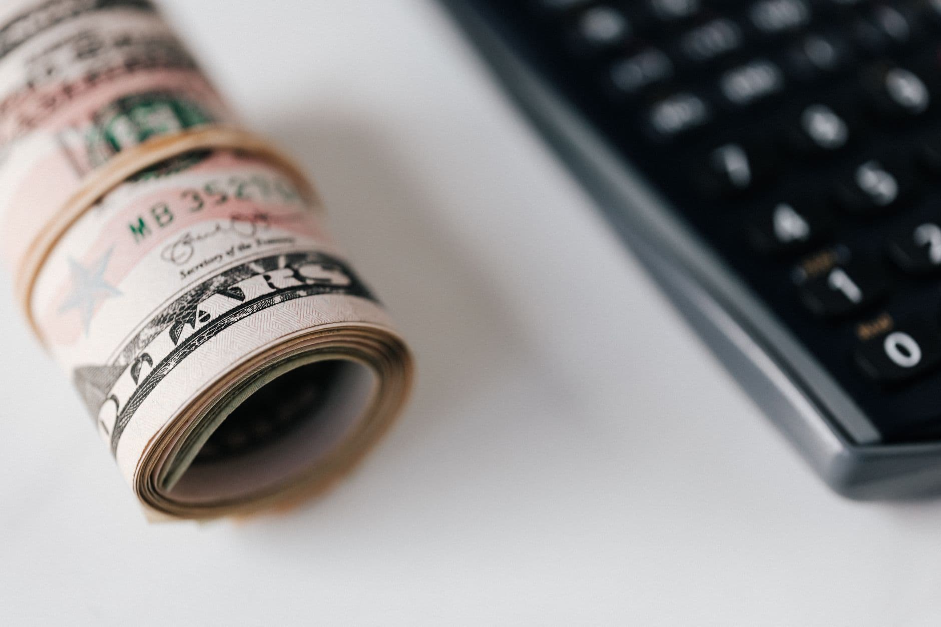 Close-up of rolled U.S. dollar bills next to a black calculator on a light surface.